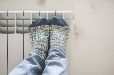 Beyaz duvarın yanındaki ısıtma kaloriferinde bacakları ısıtan adam.