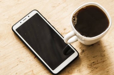 Sıcak kahve ve akıllı telefon ahşap tezgahın üstünde..