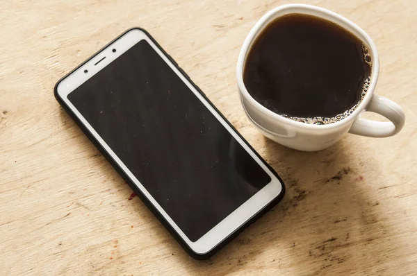 Heißer Kaffee und Smartphone auf der Holztheke. — Stockfoto