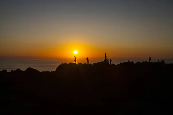 在海边的悬崖上欣赏日落的人们的剪影 — 图库照片