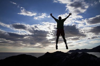 Cliff üzerinde günbatımında atlama adam silüeti. Özgürlük kavramı.