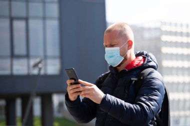 COVID-19 Pandemik Coronavirüs. SARS-CoV-2 virüsünün yayılmasına karşı maske takan akıllı telefon kullanan bir turist. 