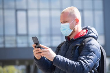 COVID-19 Pandemik Coronavirüs. SARS-CoV-2 virüsünün yayılmasına karşı maske takan akıllı telefon kullanan bir turist. 