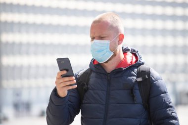 COVID-19 Pandemik Coronavirüs. SARS-CoV-2 virüsünün yayılmasına karşı maske takan akıllı telefon kullanan bir turist. 
