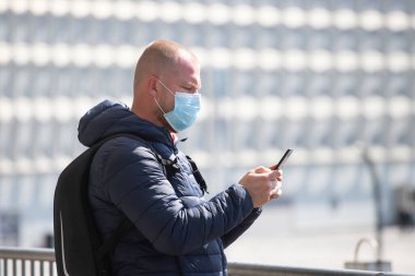 COVID-19 Pandemik Coronavirüs. SARS-CoV-2 virüsünün yayılmasına karşı maske takan akıllı telefon kullanan bir turist. 