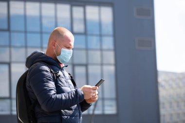 COVID-19 Pandemik Coronavirüs. SARS-CoV-2 virüsünün yayılmasına karşı maske takan akıllı telefon kullanan bir turist. 