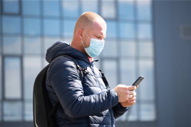 COVID-19 Pandemik Coronavirüs. SARS-CoV-2 virüsünün yayılmasına karşı maske takan akıllı telefon kullanan bir turist. 