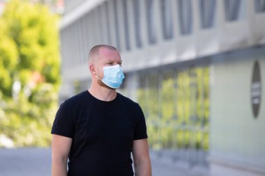 COVID-19 Pandemik Coronavirüs. Modern binanın önünde SARS-CoV-2 virüsünün yayılmasına karşı maske takan bir adam var. Koronavirüs hastalığına karşı yüzünde koruyucu maske olan bir adam..