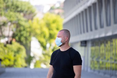 COVID-19 Pandemik Coronavirüs. Modern binanın önünde SARS-CoV-2 virüsünün yayılmasına karşı maske takan bir adam var. Koronavirüs hastalığına karşı yüzünde koruyucu maske olan bir adam..