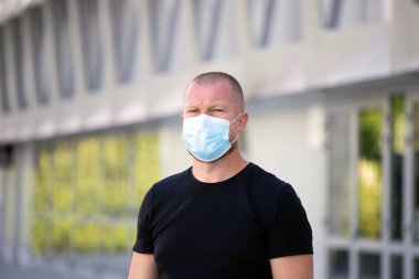 COVID-19 Pandemik Coronavirüs. Modern binanın önünde SARS-CoV-2 virüsünün yayılmasına karşı maske takan bir adam var. Koronavirüs hastalığına karşı yüzünde koruyucu maske olan bir adam..