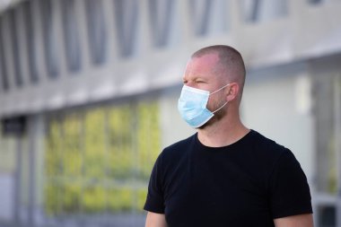 COVID-19 Pandemik Coronavirüs. Modern binanın önünde SARS-CoV-2 virüsünün yayılmasına karşı maske takan bir adam var. Koronavirüs hastalığına karşı yüzünde koruyucu maske olan bir adam..