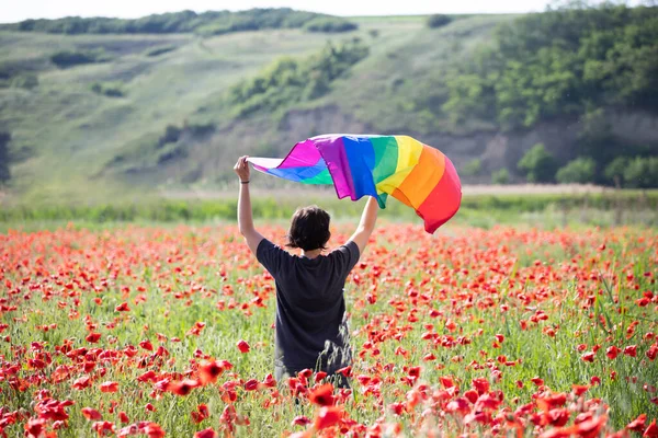 Woman holding a Gay Rainbow Flag over poppy field. Bisexual,gay, lesbian, transsexual symbol. Happiness, freedom and love concept for same sex couples