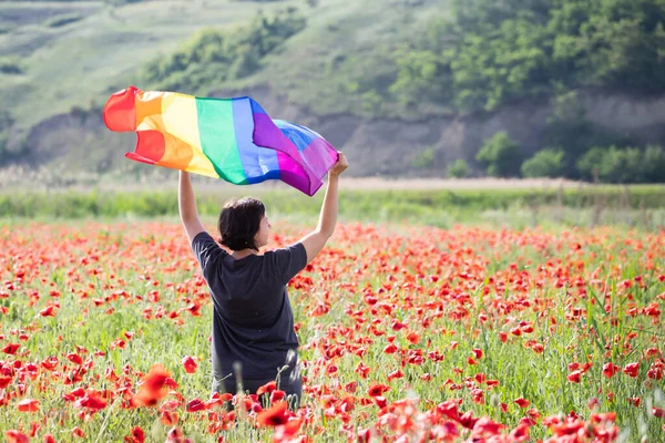 ケシ畑の上にゲイレインボーフラッグを持つ女性 バイセクシャル レズビアン トランスセクシャルのシンボル 同じセックスカップルのための幸福 自由と愛の概念 — ストック写真