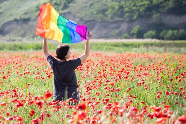 ケシ畑の上にゲイレインボーフラッグを持つ女性 バイセクシャル レズビアン トランスセクシャルのシンボル 同じセックスカップルのための幸福 自由と愛の概念 — ストック写真