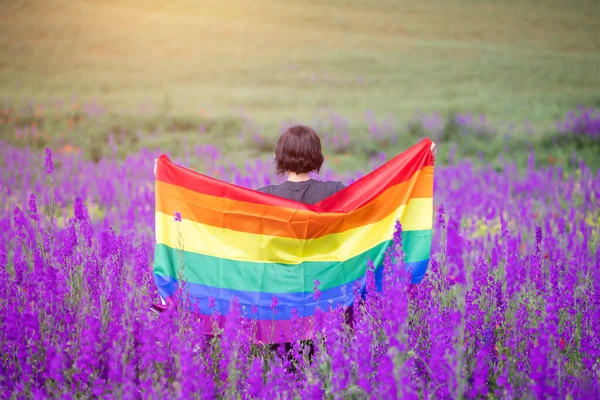 Woman holding a Gay Rainbow Flag in beautiful summer field. Bisexual,gay, lesbian, transsexual symbol. Happiness, freedom and love concept for same sex couples.