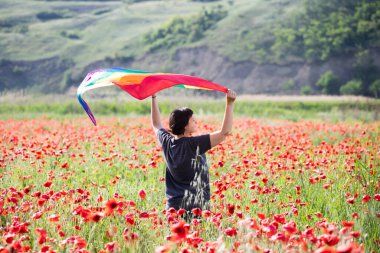 Haşhaş tarlasında elinde Gay Gökkuşağı Bayrağı olan bir kadın. Biseksüel, gey, lezbiyen, transseksüel sembolü. Aynı cinsiyet çiftleri için mutluluk, özgürlük ve aşk kavramı