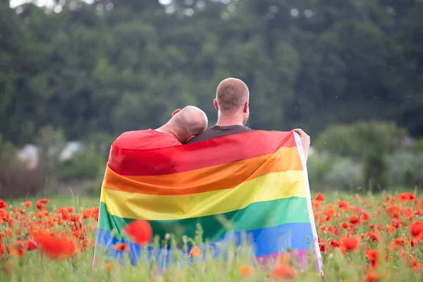 在美丽的罂粟地里 一对同性恋夫妇举着一面同性恋彩虹旗 双性恋 同性恋 女同性恋 变性人的象征 同性夫妇的幸福 自由和爱的概念 — 图库照片