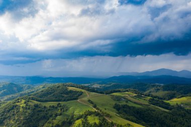 Uçan, uçsuz bucaksız otlakların yeşil tarlaları ve otlakları, arka planda fırtınalı gökyüzü.