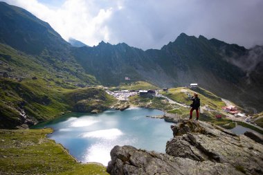 Kaya tepesinde kalan adam buzulların arasındaki güzel gölün tadını çıkarıyor..
