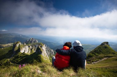 Uçurumda oturan genç çift dağ manzarasının tadını çıkarıyor. Aşk ve seyahat, mutlu duygular, yaşam tarzı konsepti.