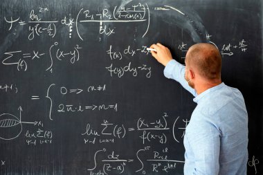 Okulda matematik dersi veren maskeli bir erkek öğretmen. Coronavirus salgını sırasında sosyal uzaklık ve sınıf güvenliği