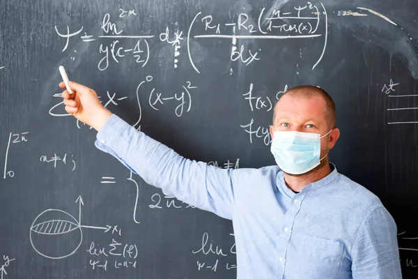 Teacher with mask teaching math lesson at school. Social distanting and classroom safety during coronavirus epidemic