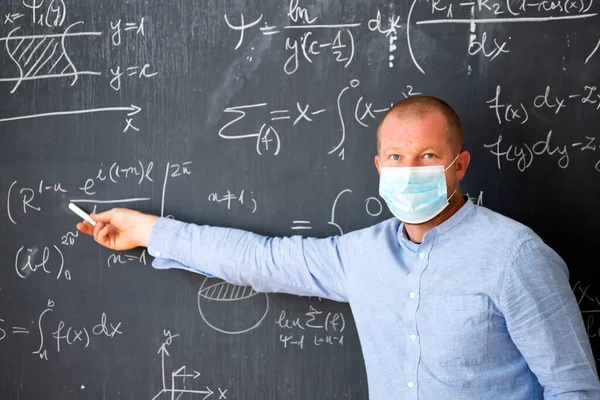 Male teacher with mask teaching math lesson at school. Social distanting and classroom safety during coronavirus epidemic