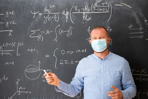 Male teacher with mask teaching math lesson at school. Social distanting and classroom safety during coronavirus epidemic