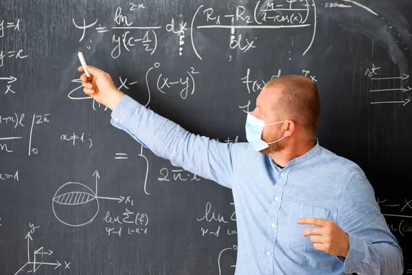 Male teacher with mask teaching math lesson at school. Social distanting and classroom safety during coronavirus epidemic