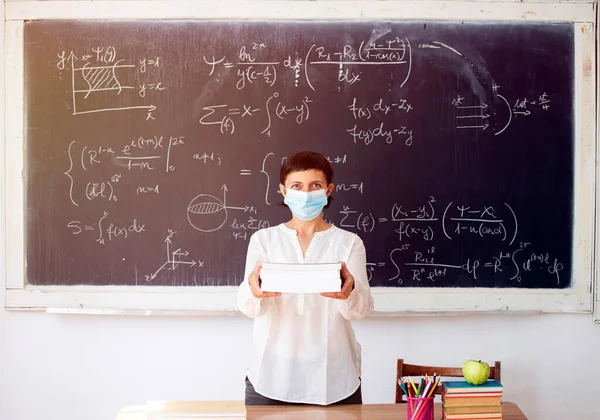 Teacher with face mask welcoming children back at school after lockdown. Back to school during COVID-19 pandemic.