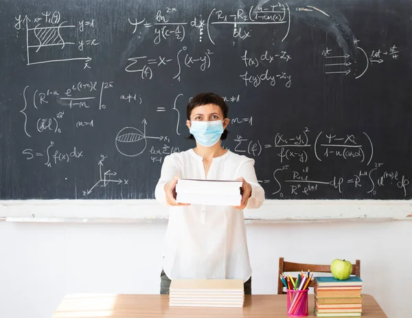 Teacher with face mask welcoming children back at school after lockdown. Back to school during COVID-19 pandemic.