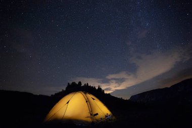 Kamp çadırı yıldızlarla dolu bir gece gökyüzünün altında parlıyor. Kamp, macera, seyahat kavramı.