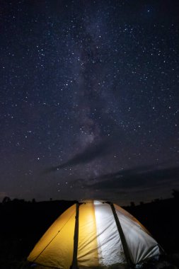 Kamp çadırı yıldızlarla dolu bir gece gökyüzünün altında parlıyor. Kamp, macera, seyahat kavramı.