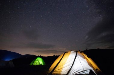 Kamp çadırı yıldızlarla dolu bir gece gökyüzünün altında parlıyor. Kamp, macera, seyahat kavramı.