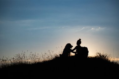 Gün batımında köpeğiyle birlikte genç bir kadının silueti..