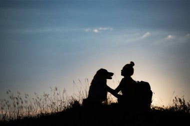 Gün batımında köpeğiyle birlikte genç bir kadının silueti..