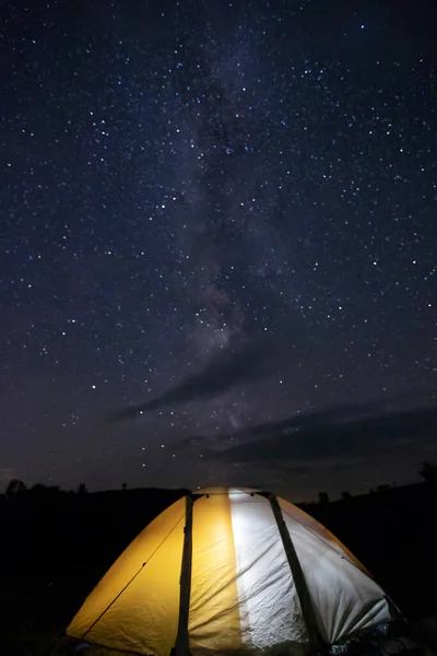 Camping tent glows under a night sky full of stars. Camping, adventure, travel concept.