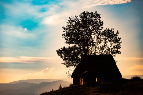 トランシルヴァニア山脈の小さな木造コテージのシルエット再び日没の空 — ストック写真