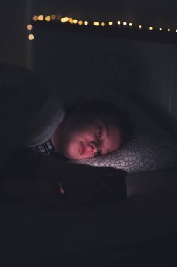 Akıllı telefon kullanan genç kız, gece geç saatte yatakta yatan tablet. Çocukların ekran bağımlılığı konsepti..