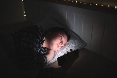 Akıllı telefon kullanan genç kız, gece geç saatte yatakta yatan tablet. Çocukların ekran bağımlılığı konsepti..