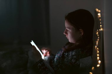 Akıllı telefon kullanan genç kız, gece geç saatte yatakta yatan tablet. Çocukların ekran bağımlılığı konsepti..