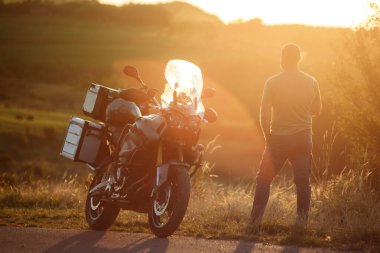 Motosiklet sürücüsü motosikletinin yanında yolda duruyor. Motosiklet konsepti gezisi ve yaşam tarzı,