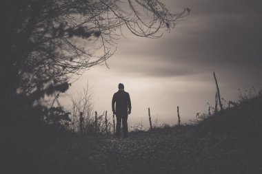 Bir adamın silueti, dikenli tellerin yanında yürüyor.