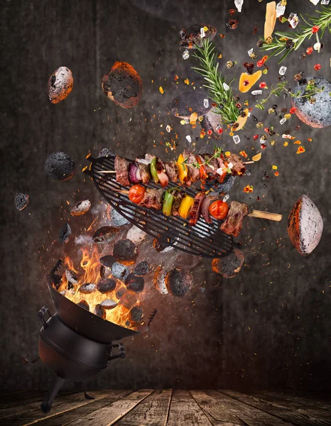 Parrilla para hervidor con briquetas calientes, rejilla de hierro fundido y sabrosos pinchos volando en el aire . — Foto de Stock