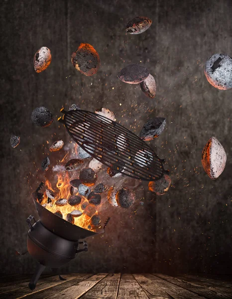 Kettle grill with hot briquettes and cost iron grid flying in the air.