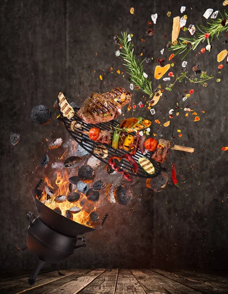 Kettle grill with hot briquettes, cast iron grate and tasty beef steaks flying in the air. — Stock Photo, Image