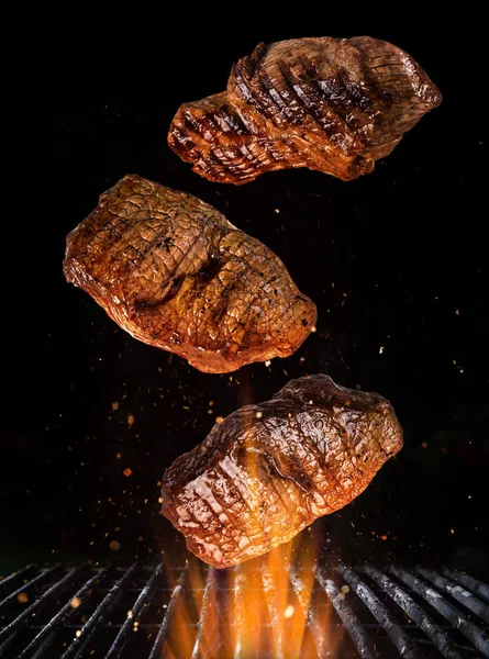 Νόστιμες μπριζόλες βοείου κρέατος που πετούν πάνω από χυτοσίδηρο σχάρα με φλόγες φωτιά. — Φωτογραφία Αρχείου