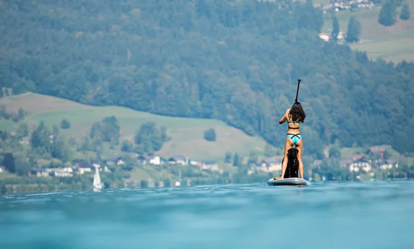 Belle femme debout sur la planche à pagaie avec son chien . — Photo