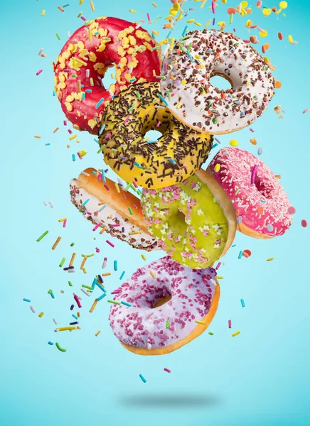 Leckere Donuts in Bewegung fallen auf pastellblauem Hintergrund. — Stockfoto