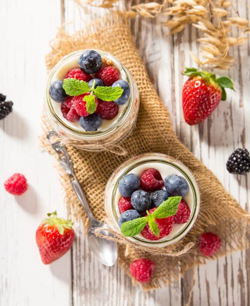 Смачні йогурти з мюслі, свіжі ягоди та варення на дерев'яному столі . — стокове фото